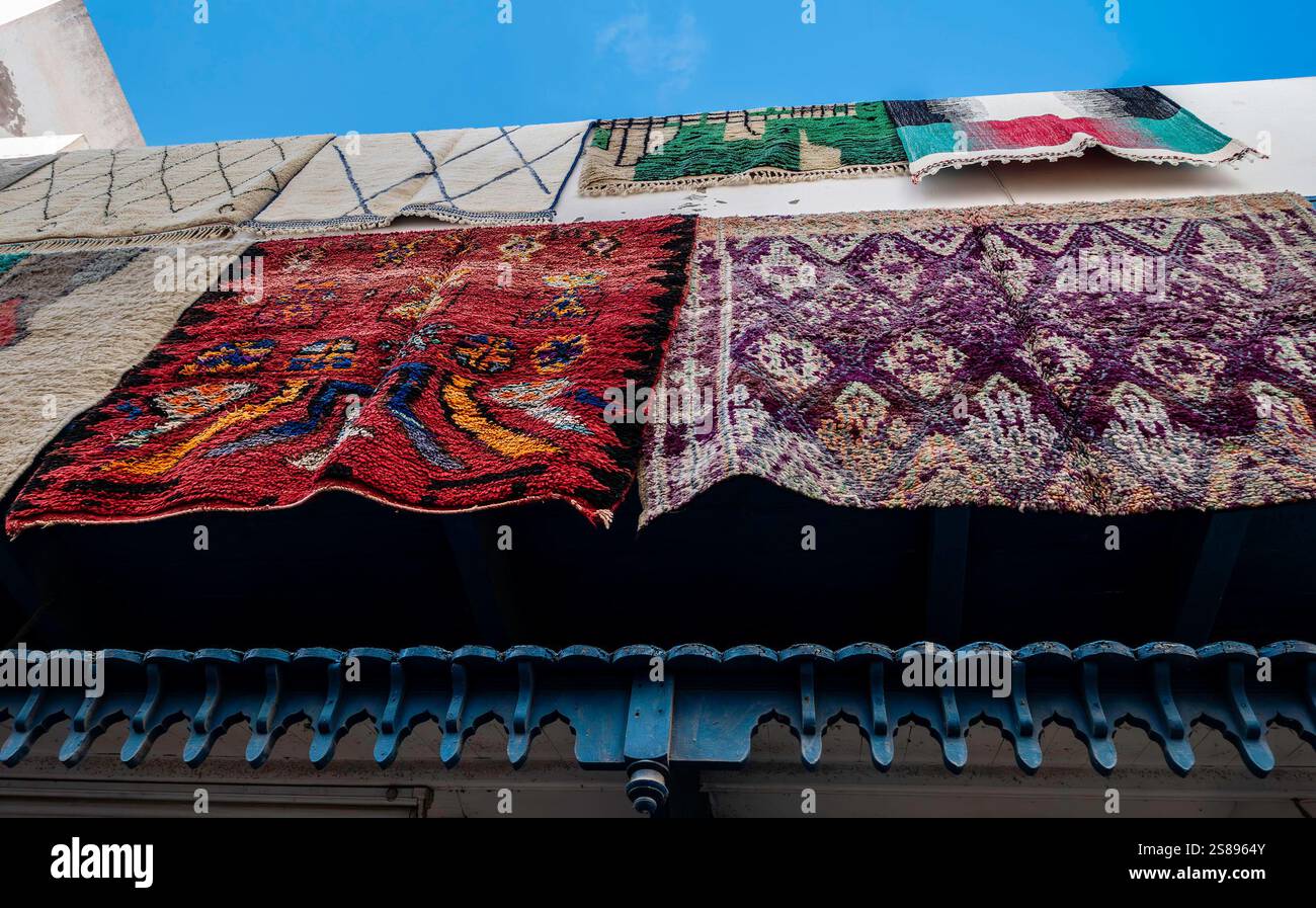 Brightly colored carpets and rugs hang prominently for sale against a building in Essaouira, Morocco, showcasing local craftsmanship. Stock Photo