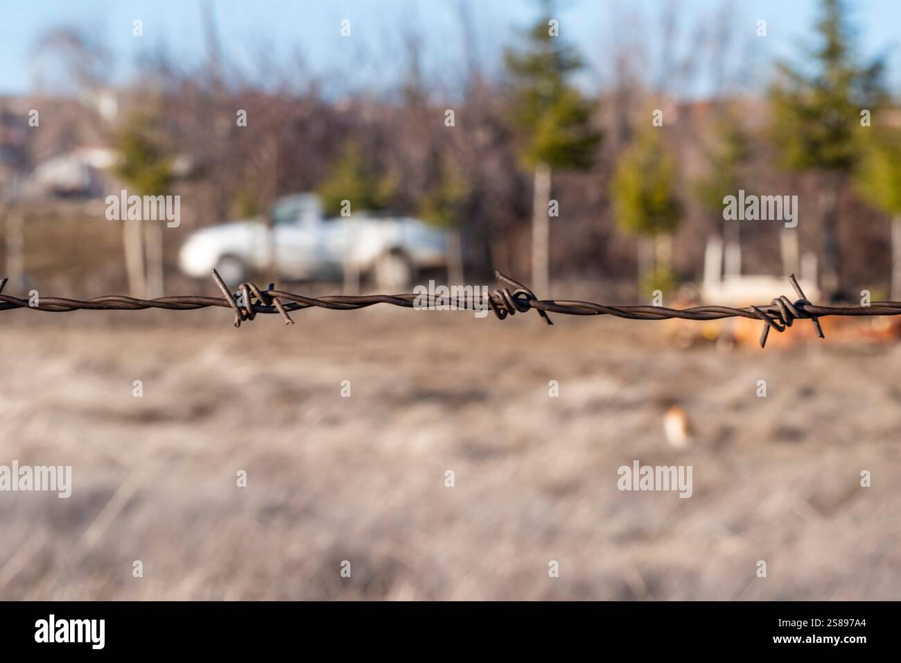 A barbed wire fence is in the foreground of a field. The fence is ...