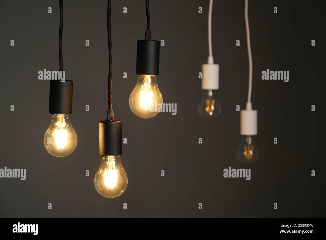 Light bulbs hanging on cords against grey background, selective focus Stock Photo