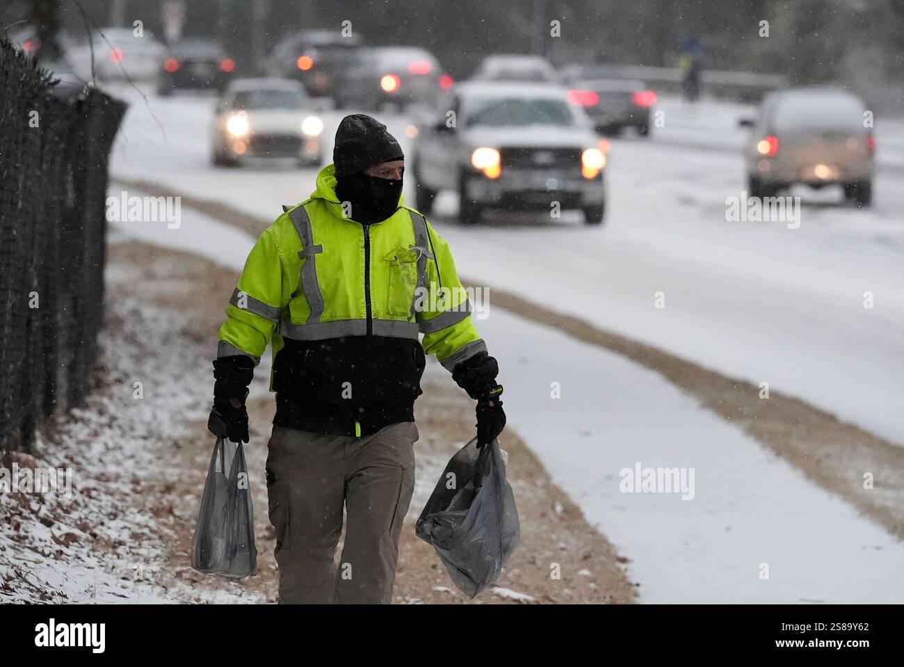 A person walks on the side walk with groceries as snow falls during a