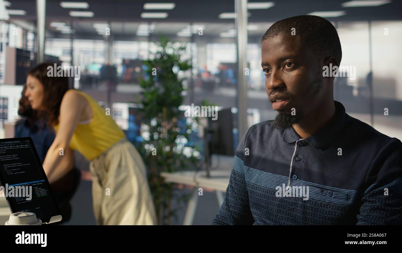 System administrator doing software quality assurance, checking source code on tablet. Close up of african american IT specialist at work inspecting coding on device, looking to fix errors, camera B Stock Photo