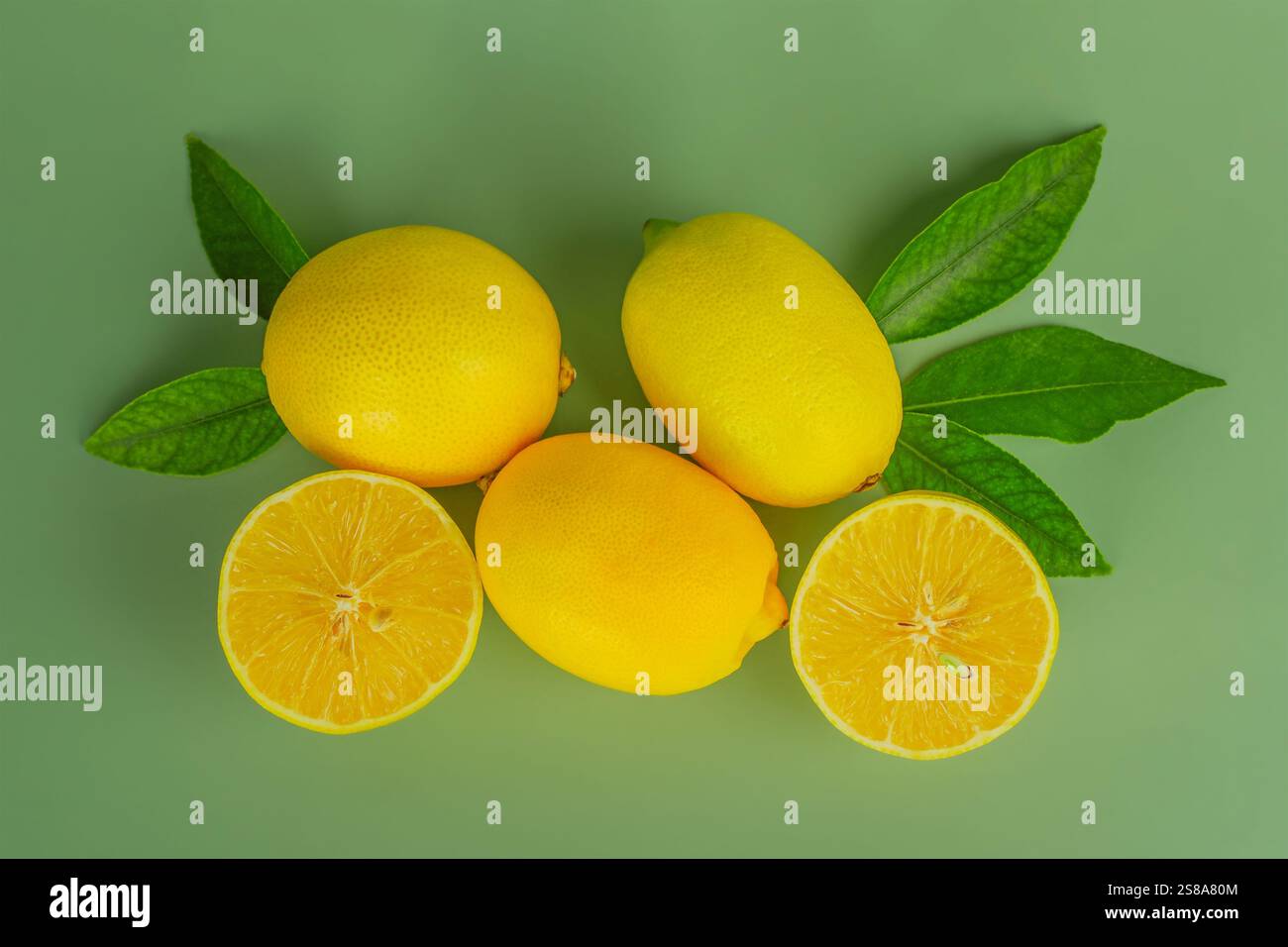Lemons whole and cut in half with leaves on a green background Stock ...