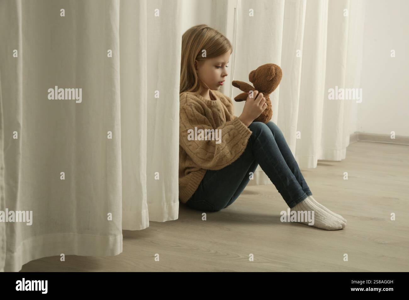 Sad and lonely little girl sitting on the floor and hugging her teddy ...