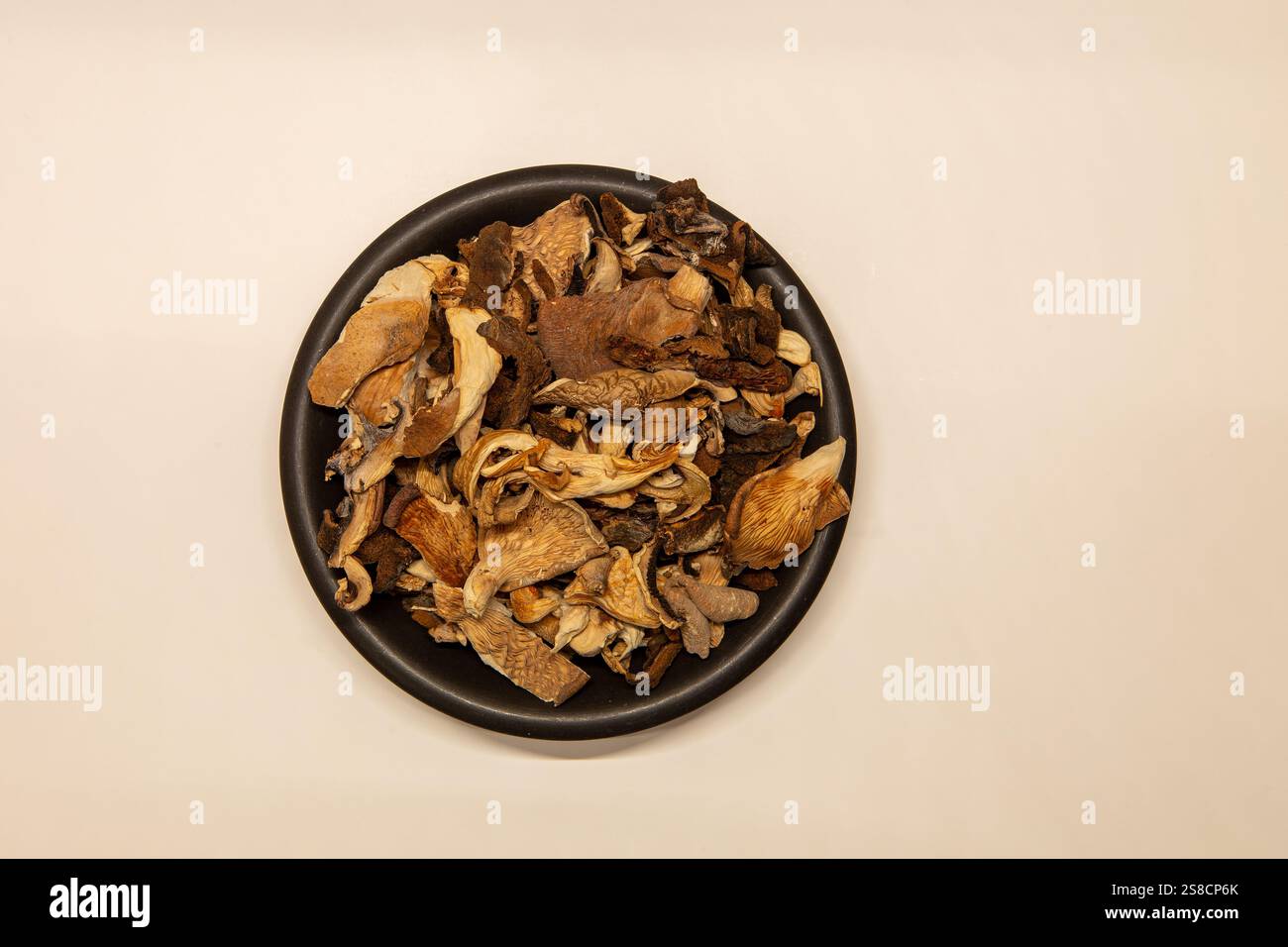 Assorted dried mushrooms on a dark ceramic plate isolated on a white background. View from above. Stock Photo