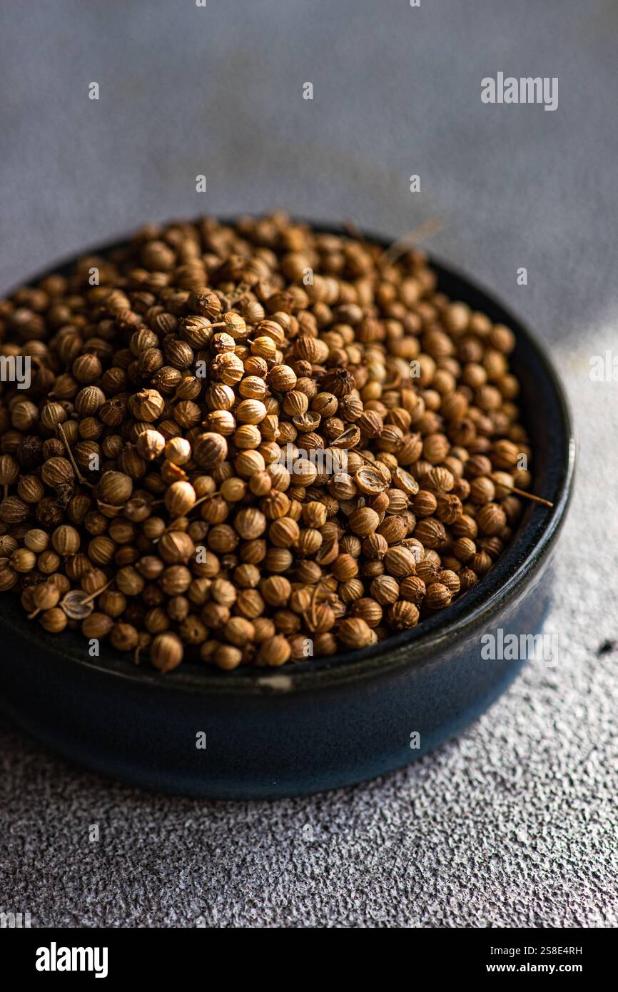 A close-up view of raw coriander seeds in a dark bowl, placed on a textured concrete table Stock Photo