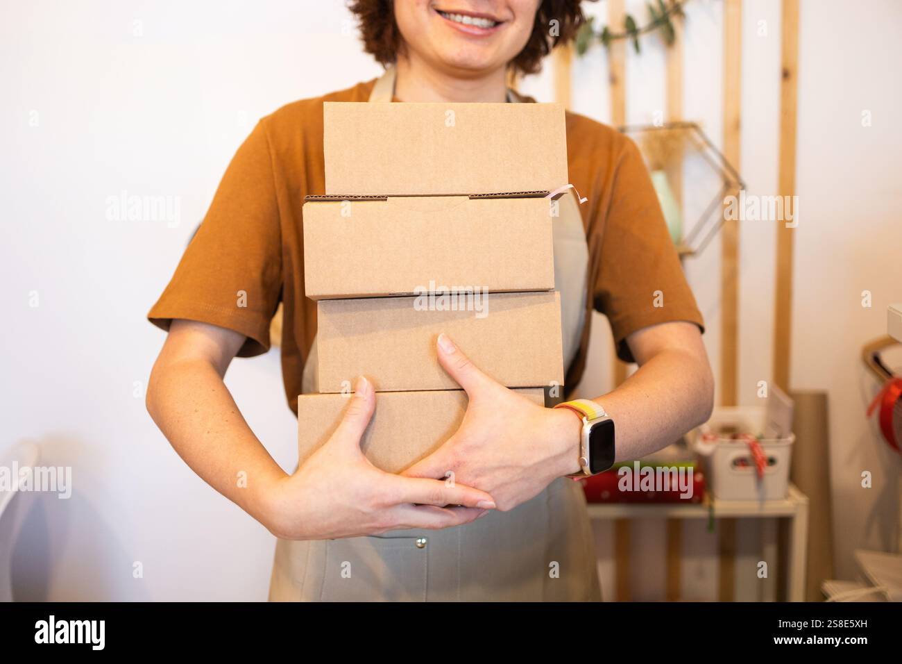A person holds a stack of cardboard boxes, smiling in a shop room The ...