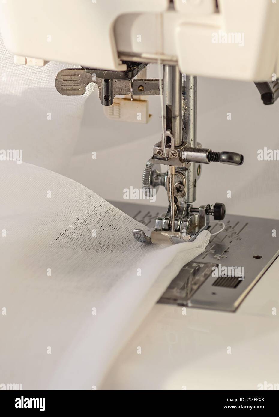Detailed close-up of a sewing machine in action, stitching a delicate white sheer fabric. The needle and thread are precisely sewing the material, sho Stock Photo