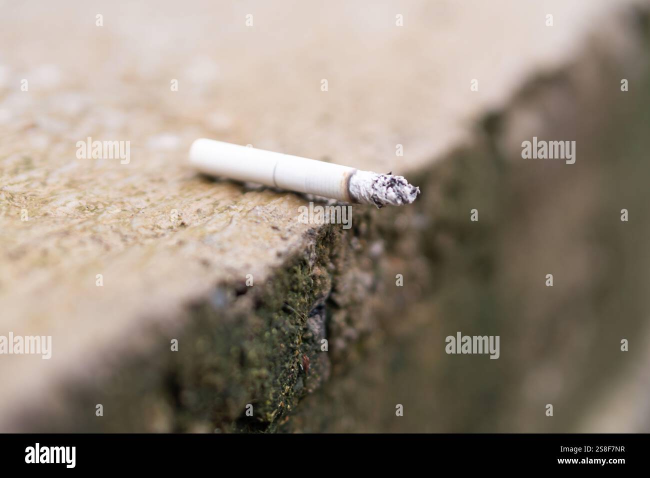 discarded cigarette A close-up of a discarded cigarette resting on a rough surface, showcasing  the ash and filter Stock Photo