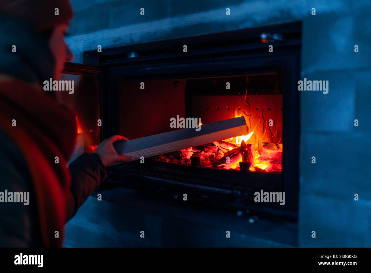 Woman adding wood to freshly installed fireplace in newly built house. Close up of fire. Creating cozy home Stock Photo