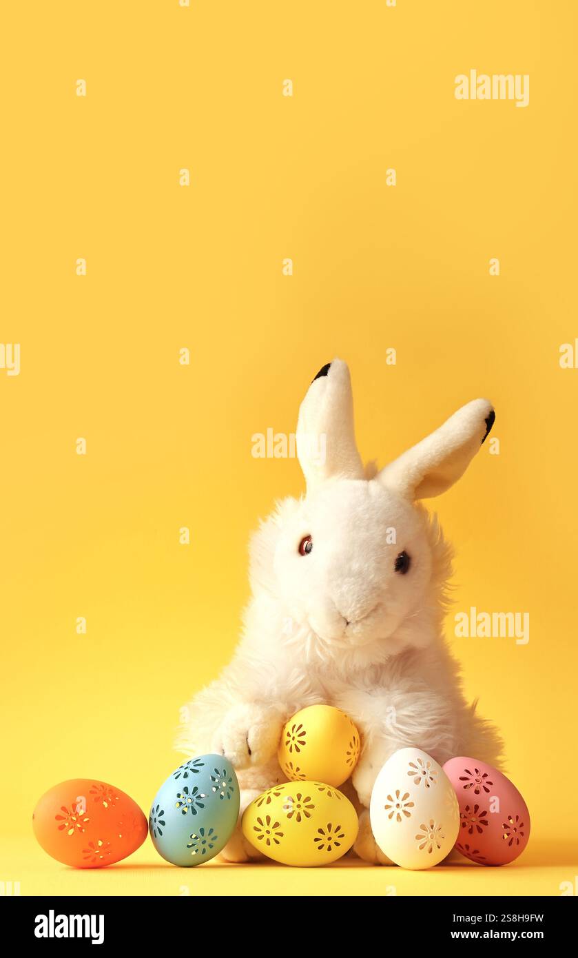 Easter bunny with colorful easter eggs on a yellow background. Stock Photo