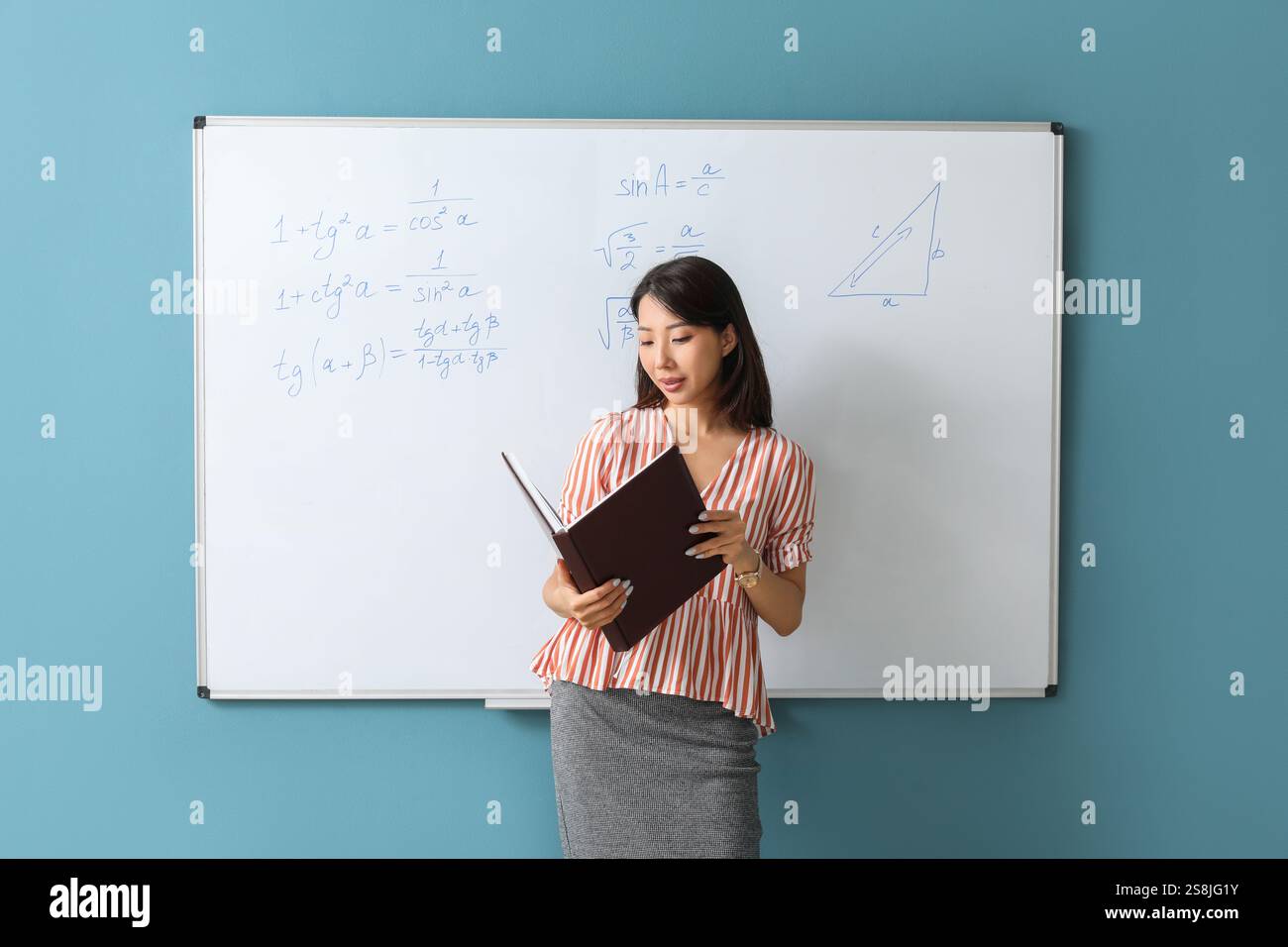 Asian Math teacher with book near flipboard in classroom Stock Photo ...