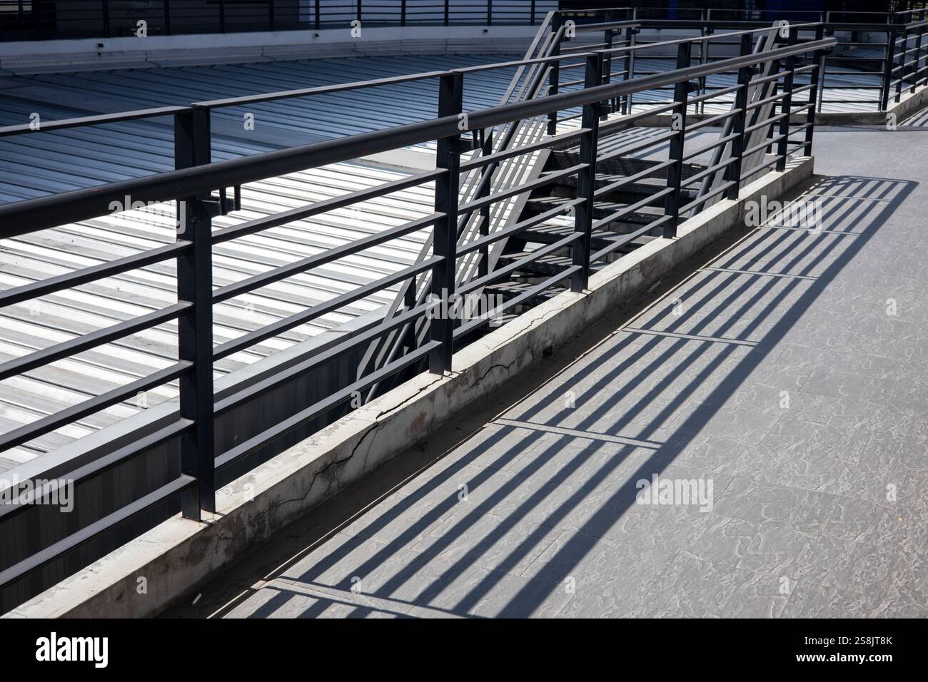 A modern black metal railing and black metal ladder, with a long shadow ...