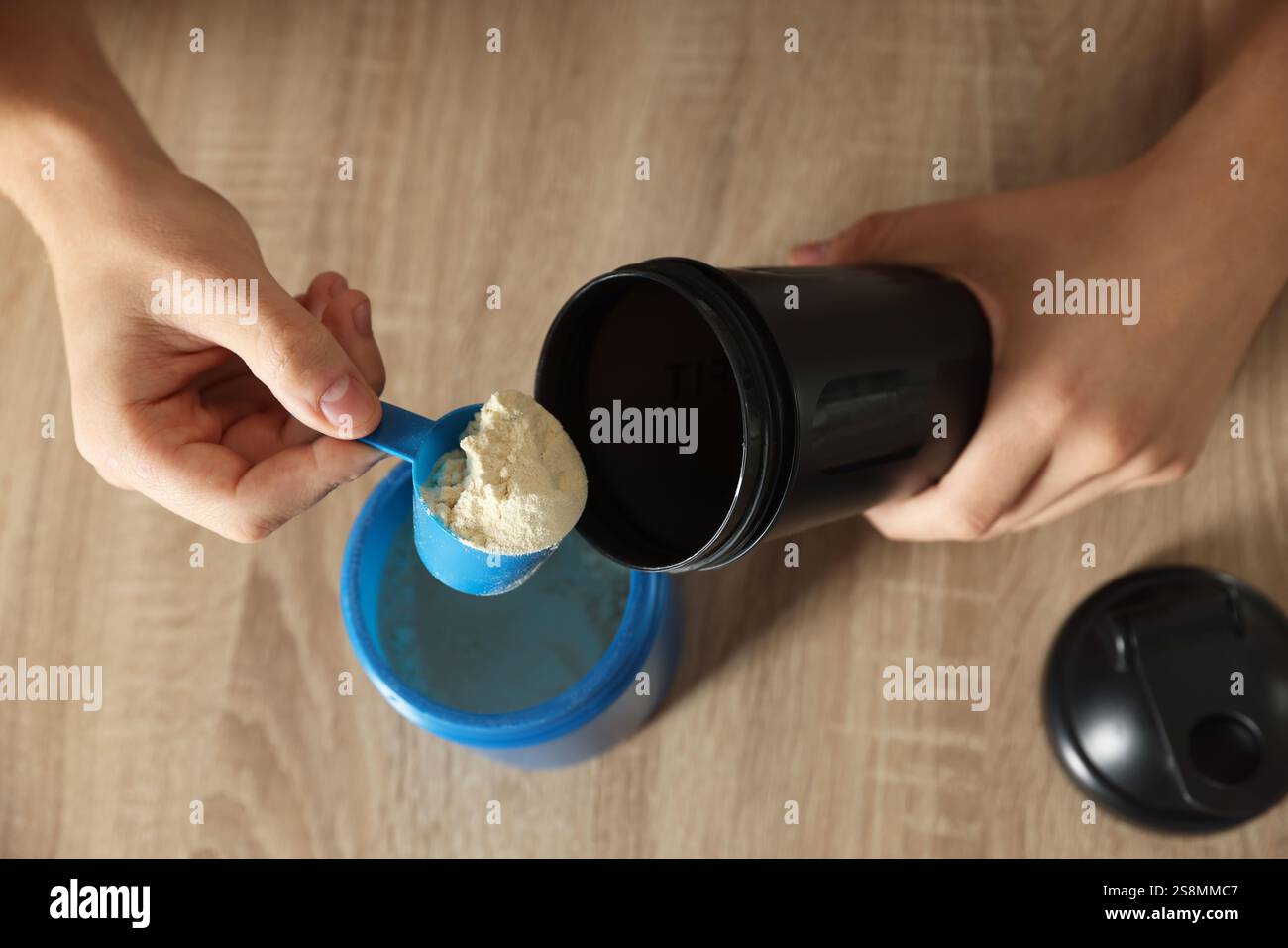 Making protein cocktail. Man adding powder into shaker at wooden table ...