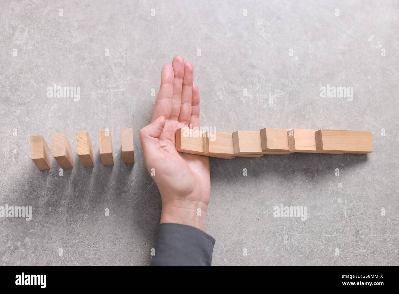 Woman stopping wooden blocks from falling on grey background, top view ...