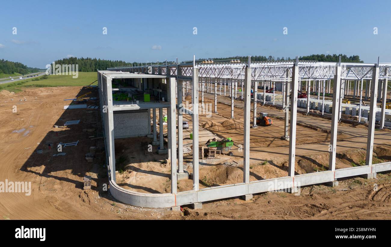 Aerial view of a construction site featuring a large building framework. The site is surrounded by open land and trees, with construction equipment vi Stock Photo