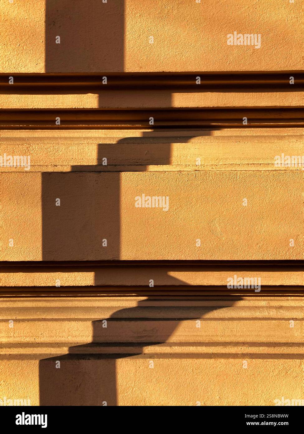 A minimalistic composition showcasing geometric shadows projected on a textured yellow stucco wall, illuminated by warm sunlight. - Smartphone Captured Stock Image