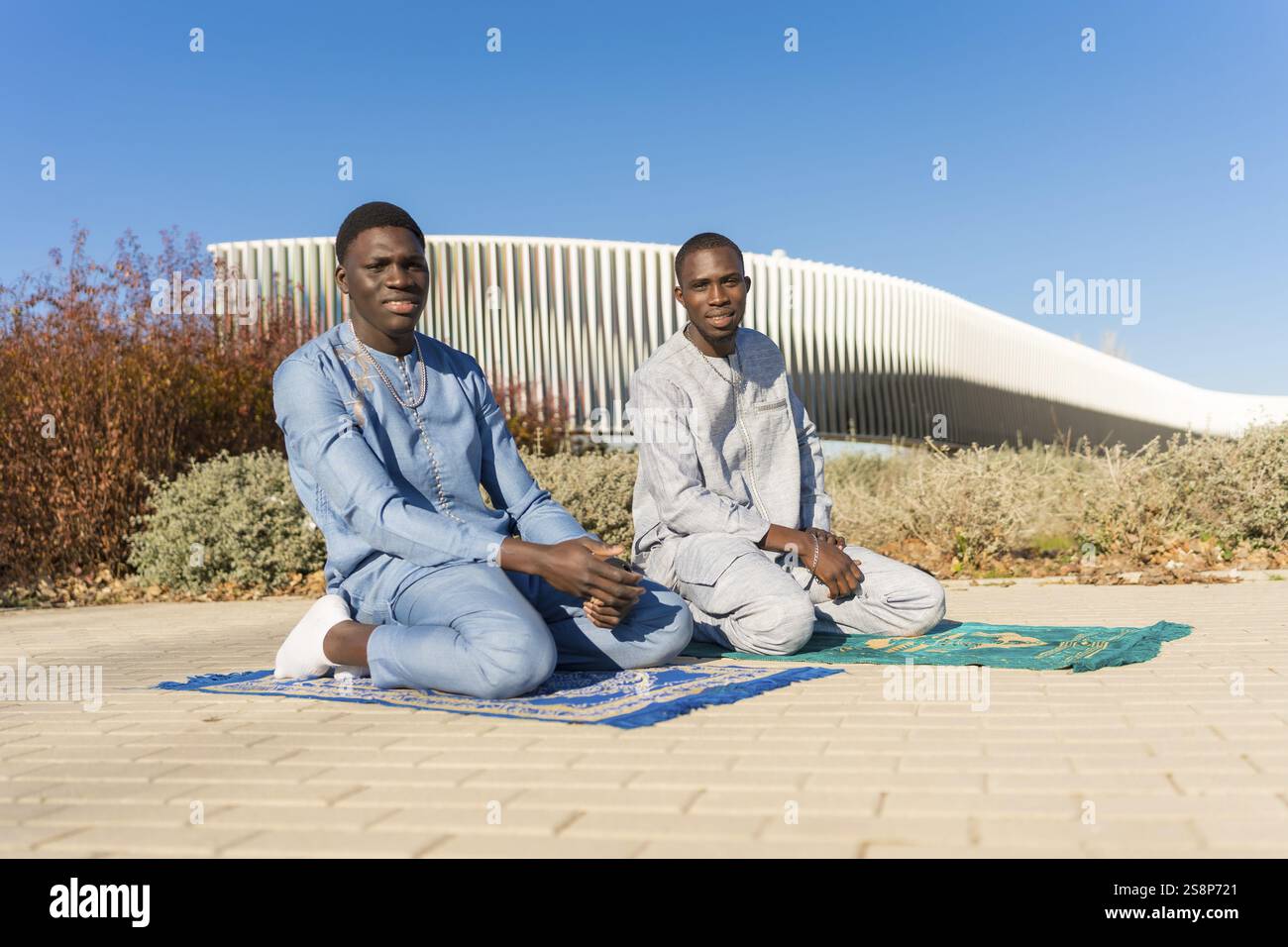 Two young senegalese men kneeling on prayer rugs and praying outdoors ...