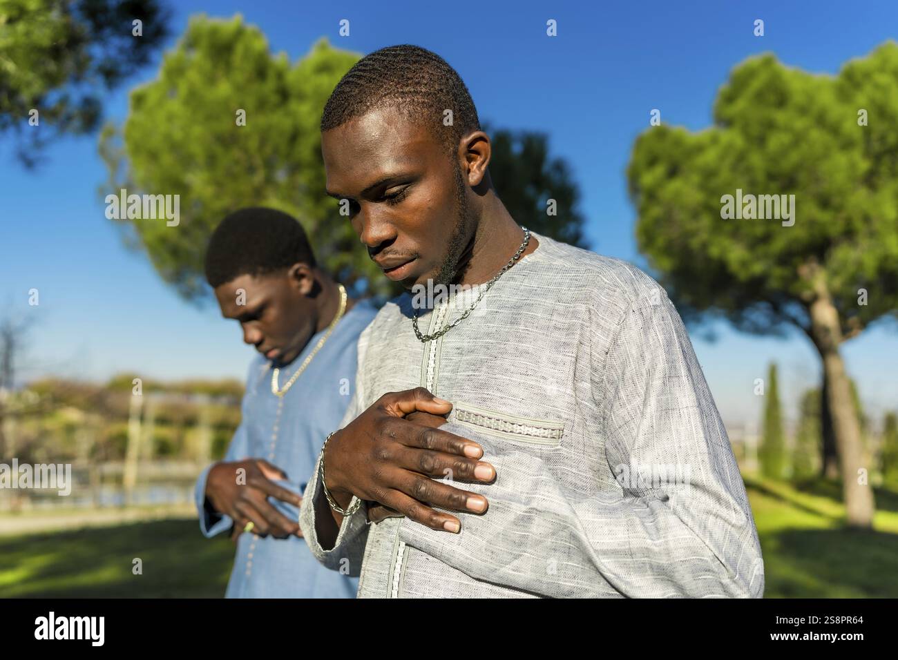 Two senegalese men wearing traditional grand boubou are praying in a park during the holy month of ramadan Stock Photo