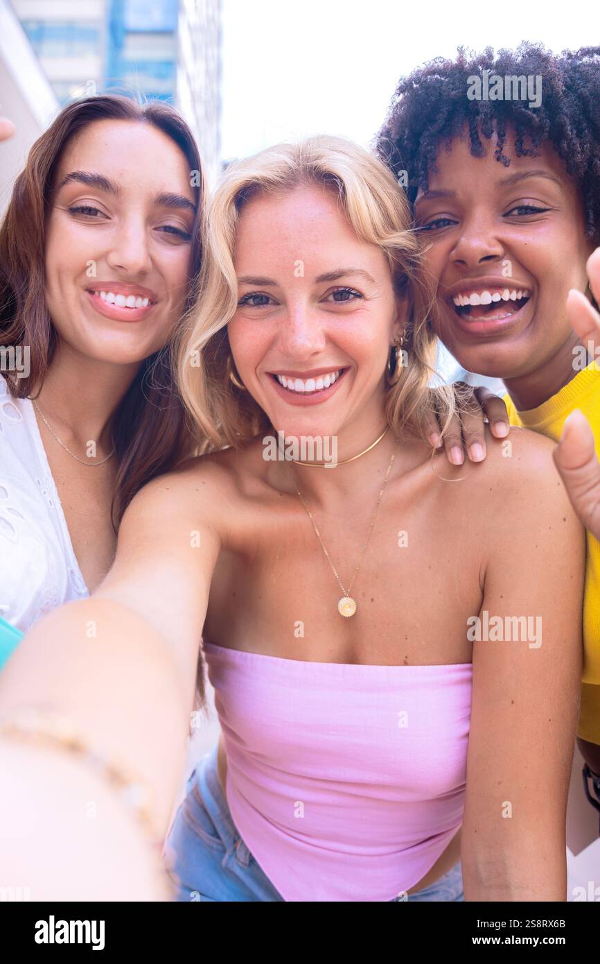 Three happy young women taking a selfie together in a city street ...