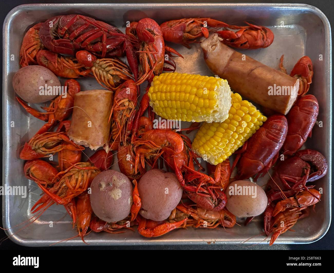 A 1 lb. crawfish boil is shown on a metal tray, served along with potatoes, corn on the cob, and sausage, as part of the Cajun cuisine in New Orleans. - Smartphone Captured Stock Image