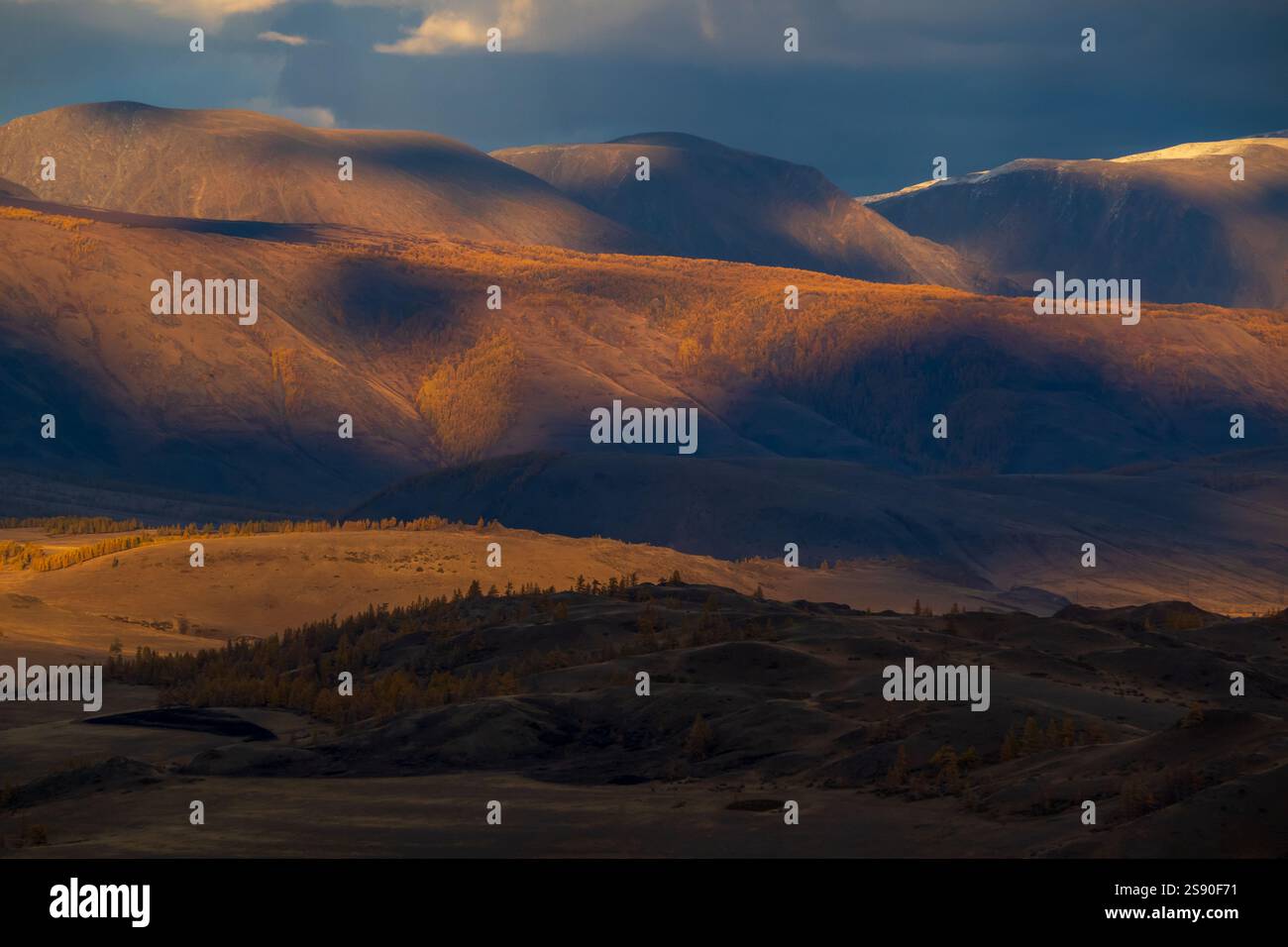 Golden light illuminates rugged mountains under a captivating sky creating a stunning scene. Stock Photo