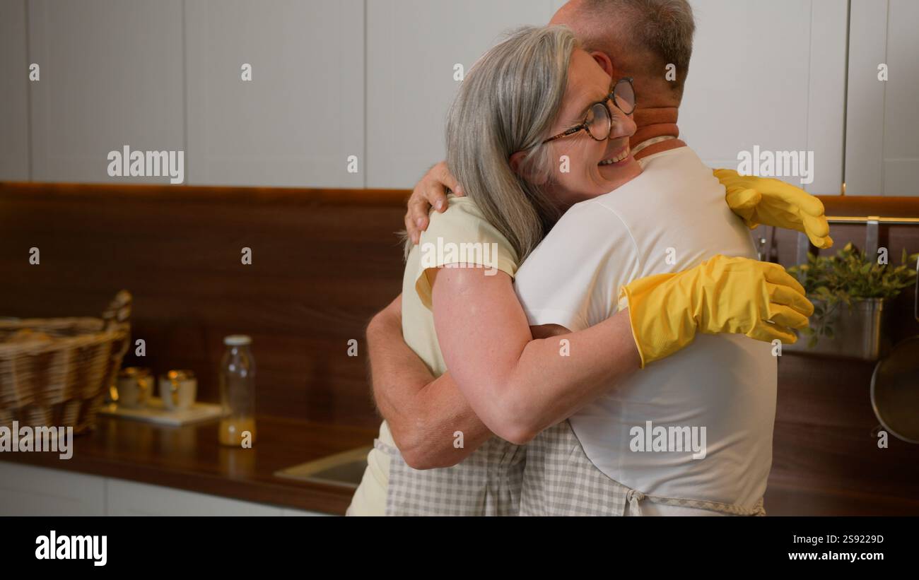 Mature wife dancing with middle-aged husband old retired couple in love having fun listen music funny dance together in kitchen washing dishes Stock Photo