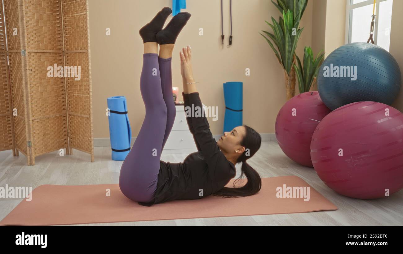 Woman exercising indoors in a gym, performing leg raises on a mat ...