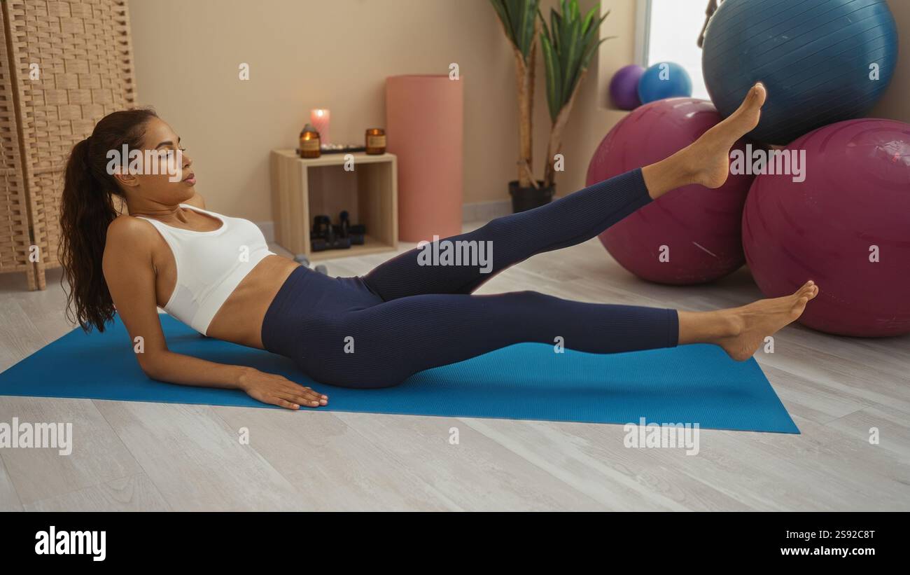 Young woman exercising on a yoga mat in a gym with fitness balls and ...