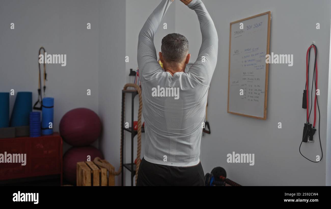 Man stretching indoors in a gymnasium with fitness equipment, ropes ...