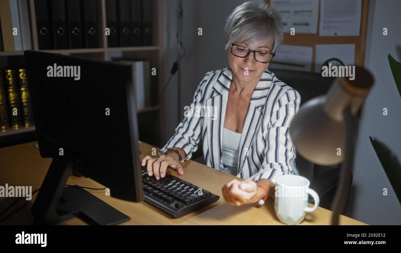 Woman with grey hair in office working at computer, holding credit card ...