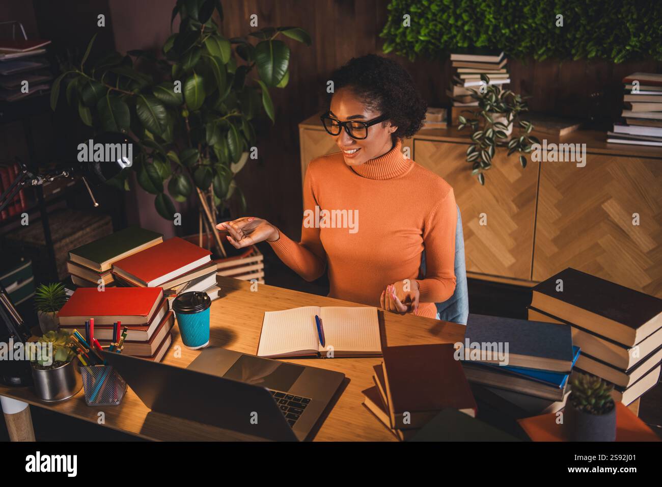 Young woman studying at home with books and laptop, wearing a casual ...