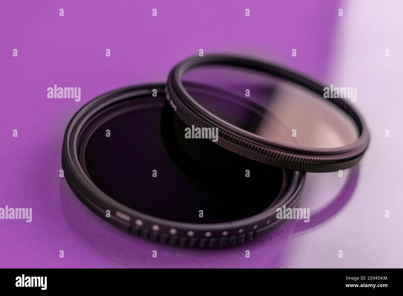Two camera lens filters, including a UV and polarizing filter, placed on a reflective purple background. Essential accessories for improving photograp Stock Photo