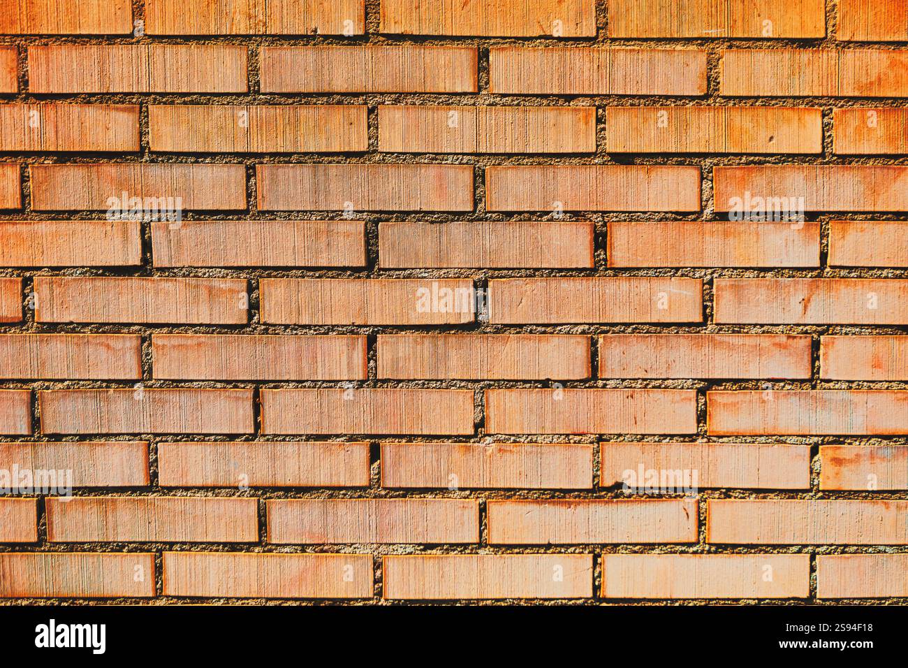 Textured brick wall with a consistent pattern of rectangular bricks arranged horizontally and vertically. The bricks are red light in color Stock Photo
