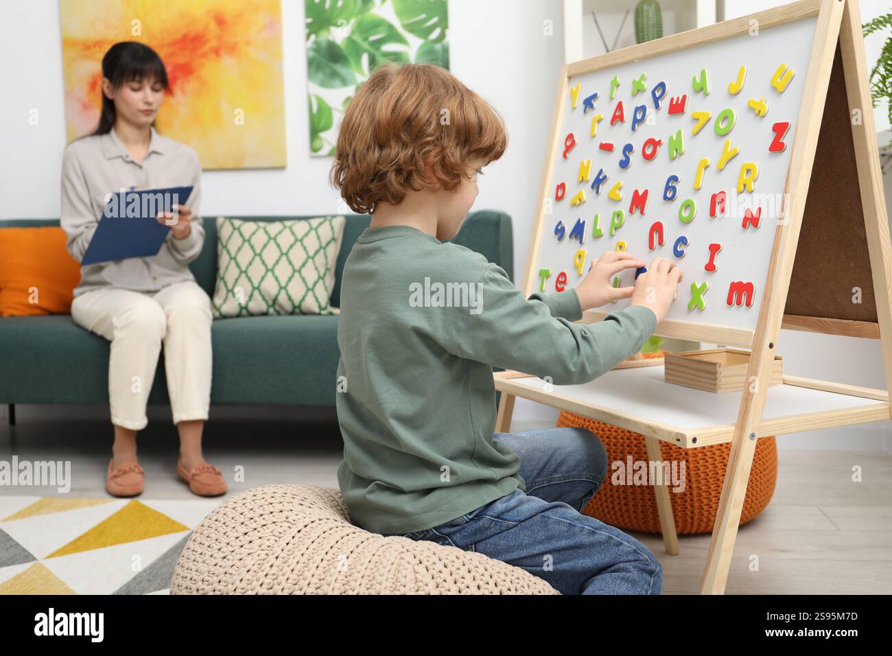 Boy assembling letters on magnetic board while psychologist taking ...