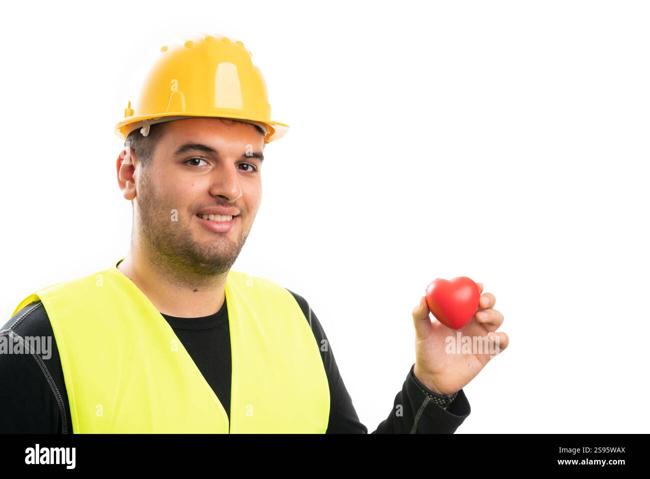 Smiling male constructor wearing yellow hardhat and fluorescent vest holding red heart as love care symbol with blank copyspace for advertising isolat Stock Photo