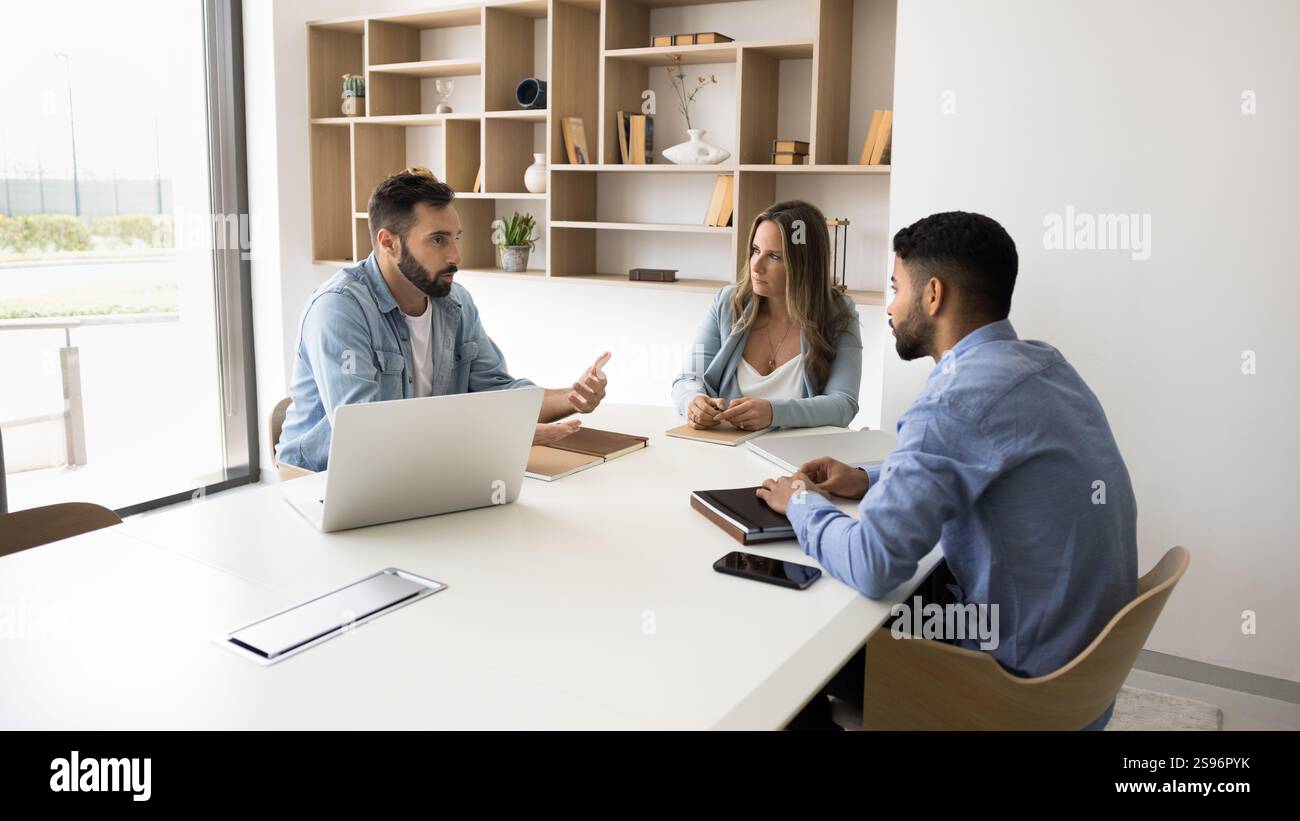 Three professionals sit at conference table engaged in discussion Stock Photo