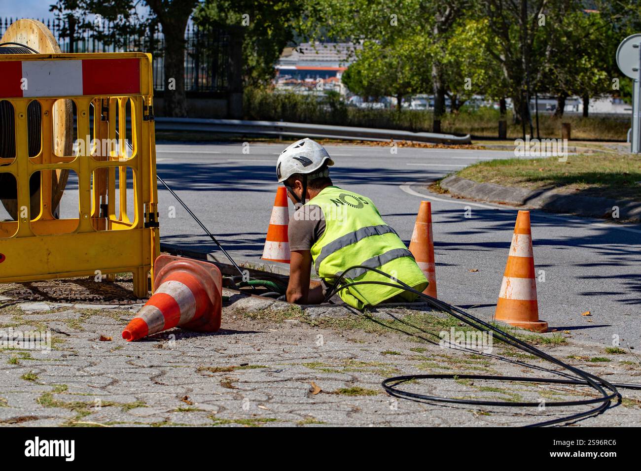 Darque, Portugal - September 12, 2024: Construction worker in a reflective vest working on underground cable installation with traffic cones Stock Photo