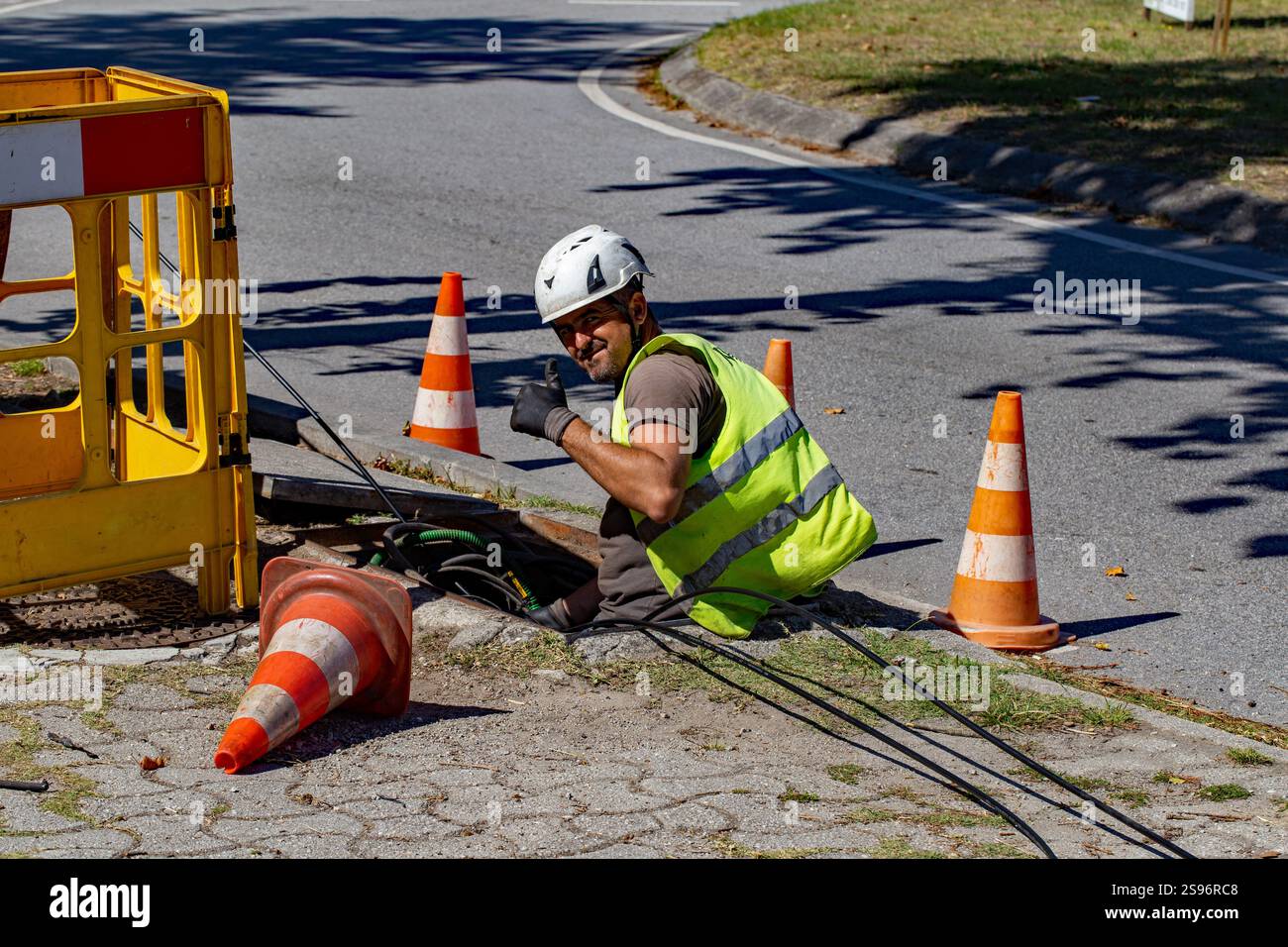 Darque, Portugal - September 12, 2024: Construction worker in a reflective vest giving a thumbs-up while working on underground cable installation wit Stock Photo