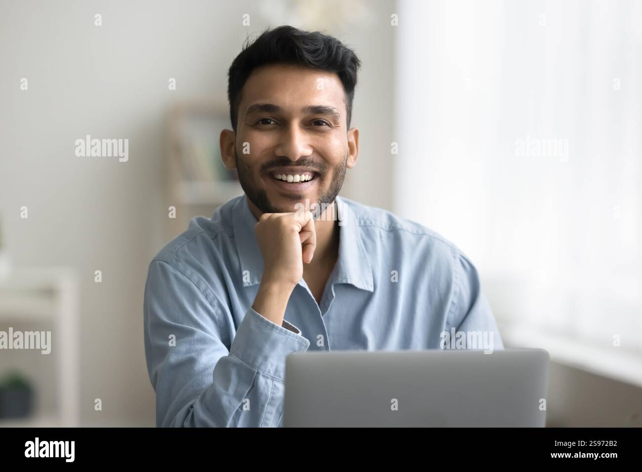 Portrait happy smiling young man sitting at workplace by notebook Stock Photo
