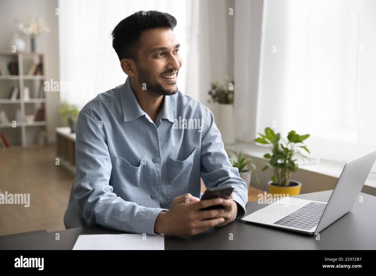 Smiling young man communicating on phone at workplace use notebook Stock Photo