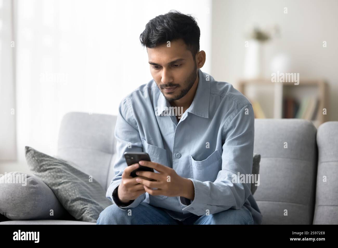 Young man sitting on sofa using cellphone for online work Stock Photo