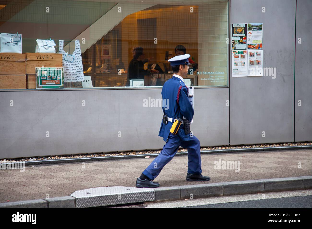 A Japanese policeman doing stretches exercises on the sidewalk in Ginza ...