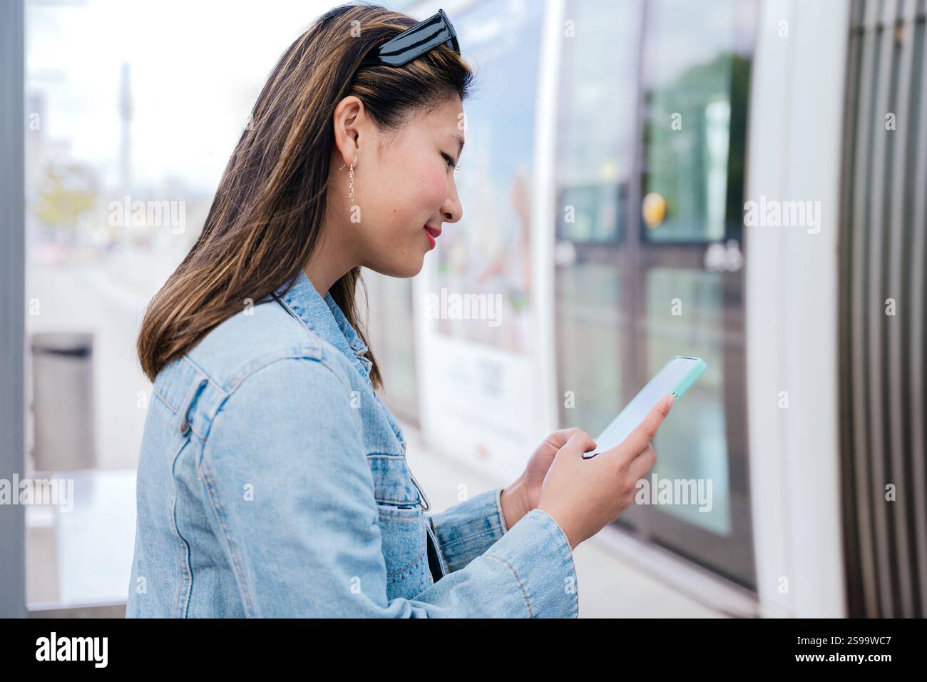 Young Woman Using Smartphone While Waiting for Tram to Board Stock Photo