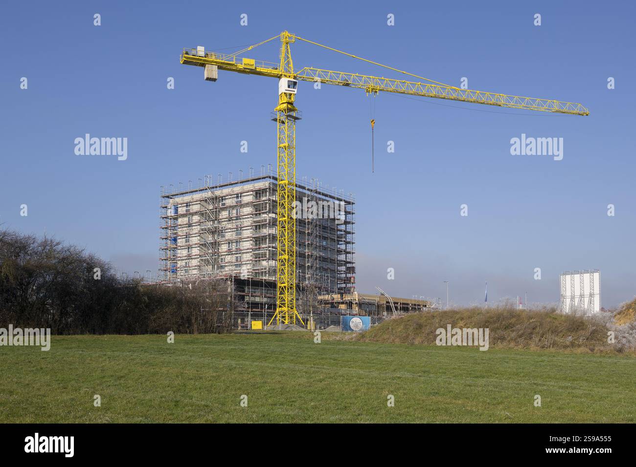 Building under construction behind overgrown hill, with crane and clear sky, residential construction, new construction of 50 flats, new development a Stock Photo