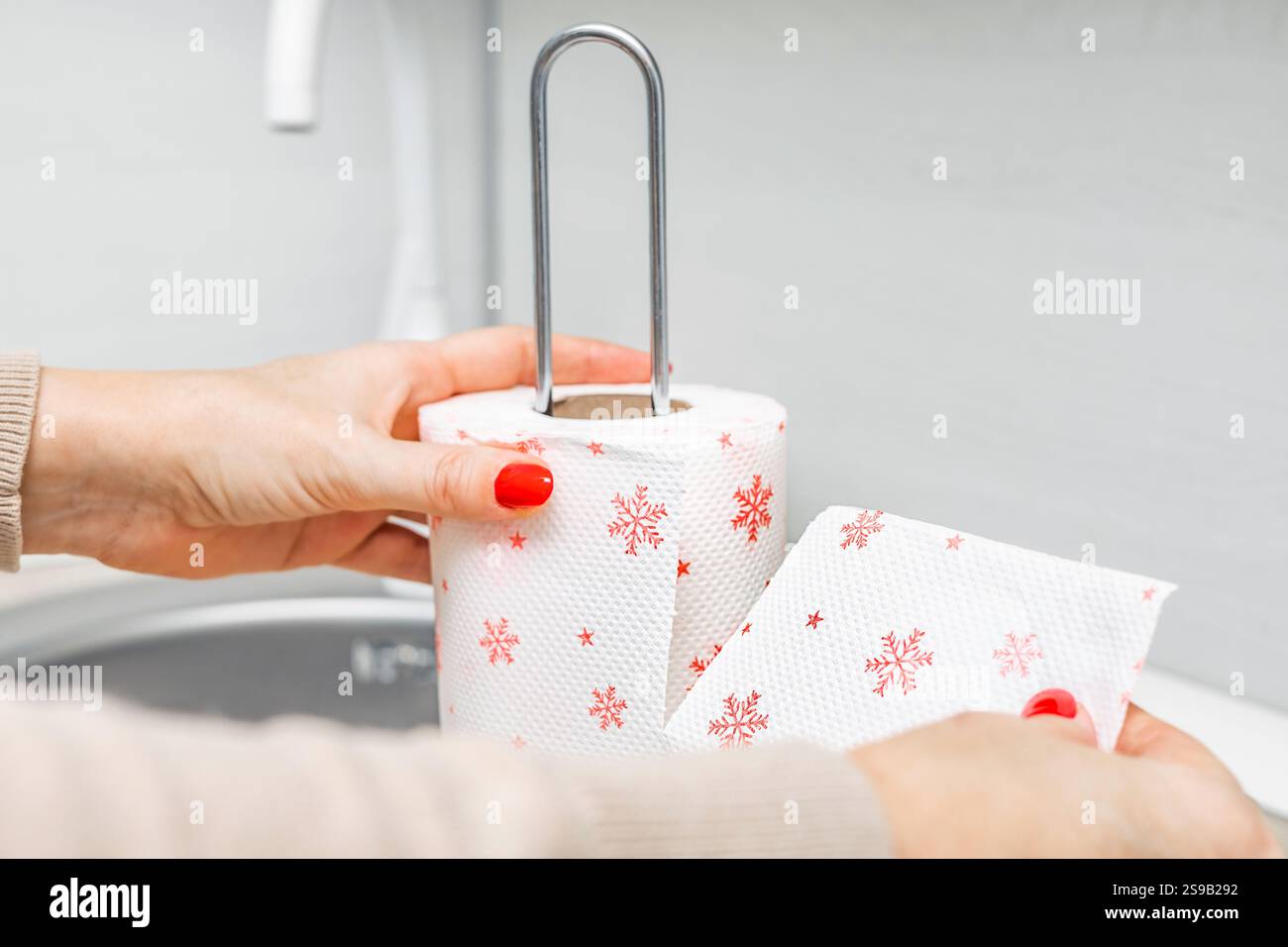 woman's hand ripping off paper towel in kitchen. roll of paper towel in the kitchen. towel with snowflakes. red snowflakes. break line. Stock Photo