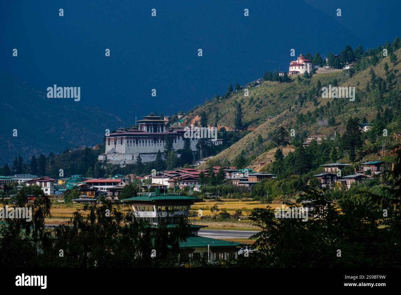 Imposing structure of Paro Dzong rises above Paro town.  Above, the National Museum of Bhutan catches the last rays of setting sun Stock Photo