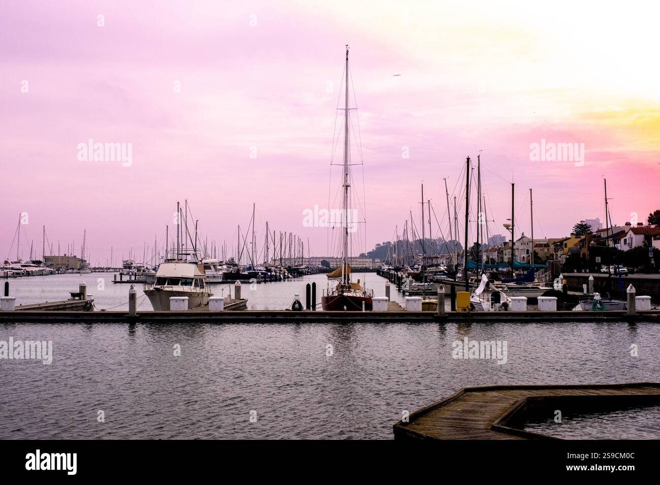 Sailboats are anchored in a calm marina as a vibrant sunset paints the ...