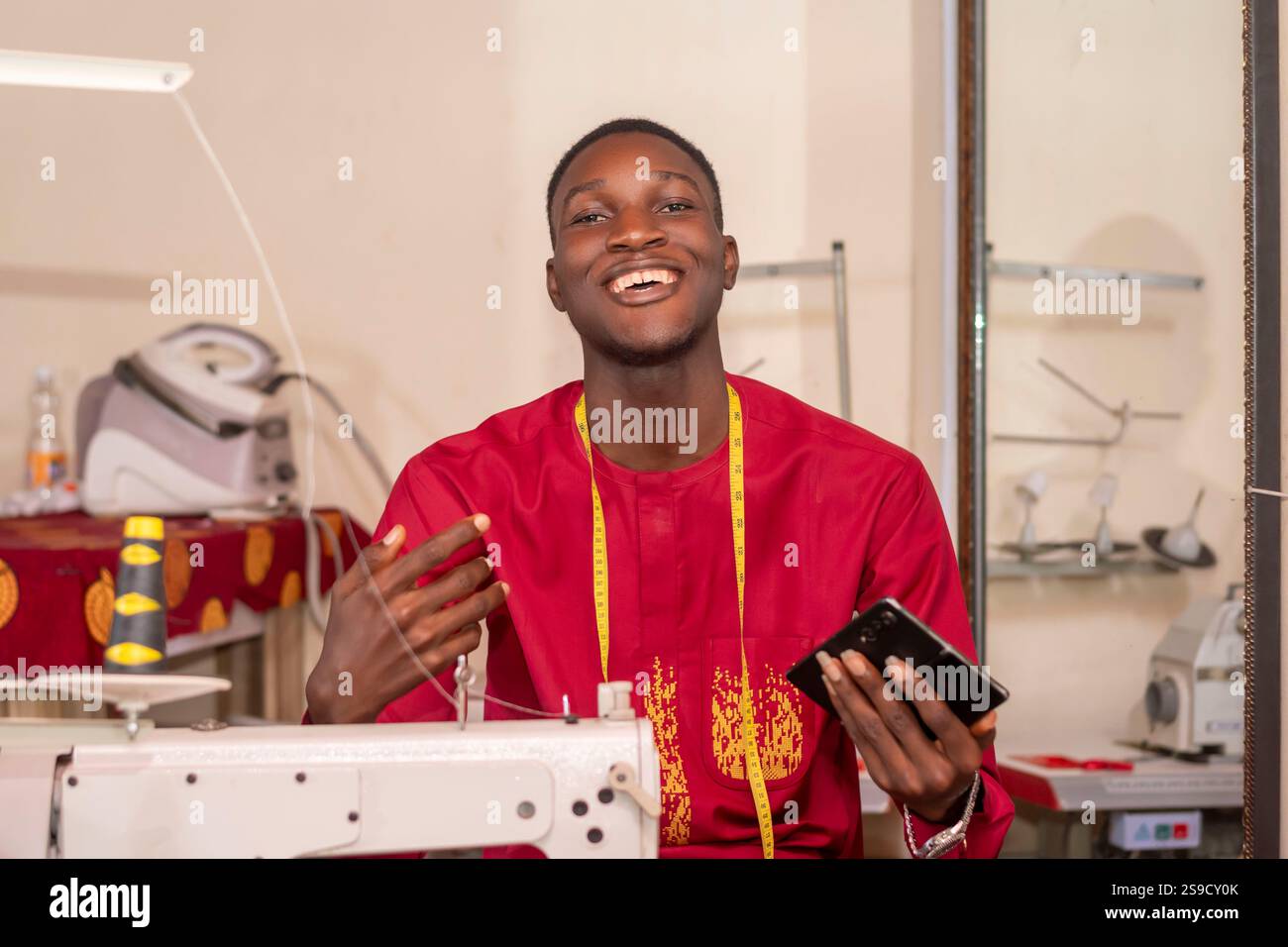 An African tailor using his phone while working in his workshop. Stock Photo