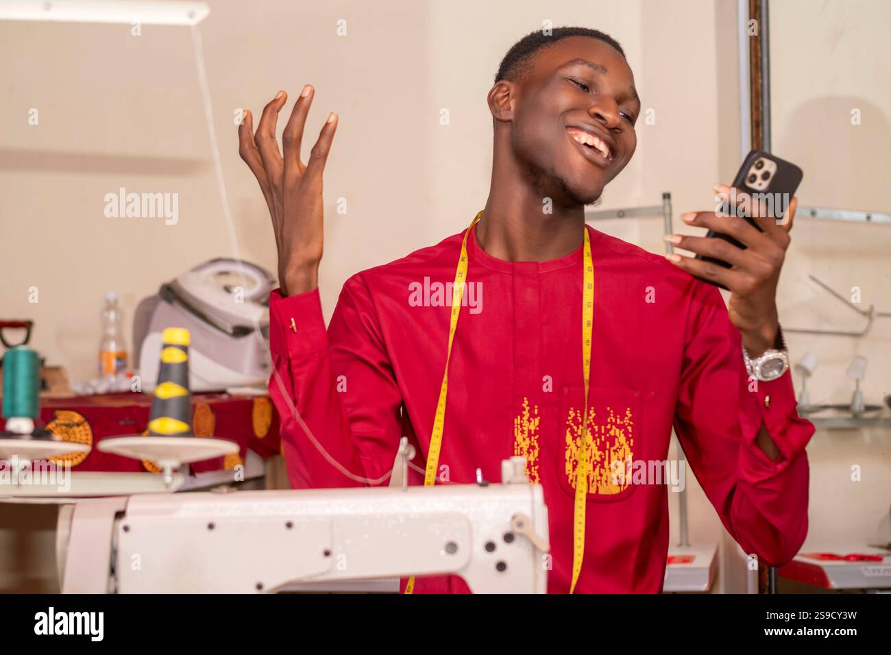 An African tailor using his phone while working in his workshop. Stock Photo