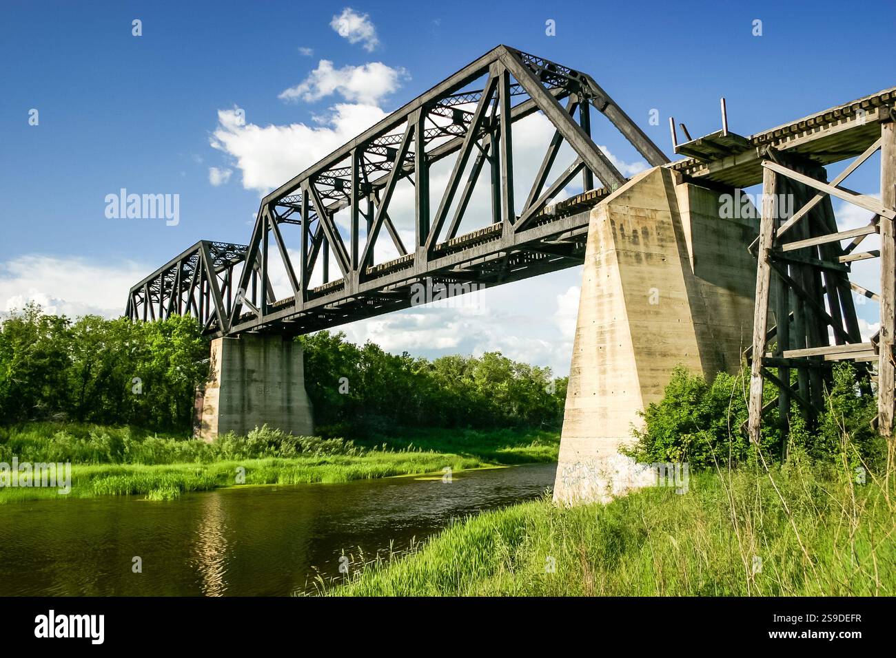 A bridge spans a river with a green grassy bank on either side. The ...